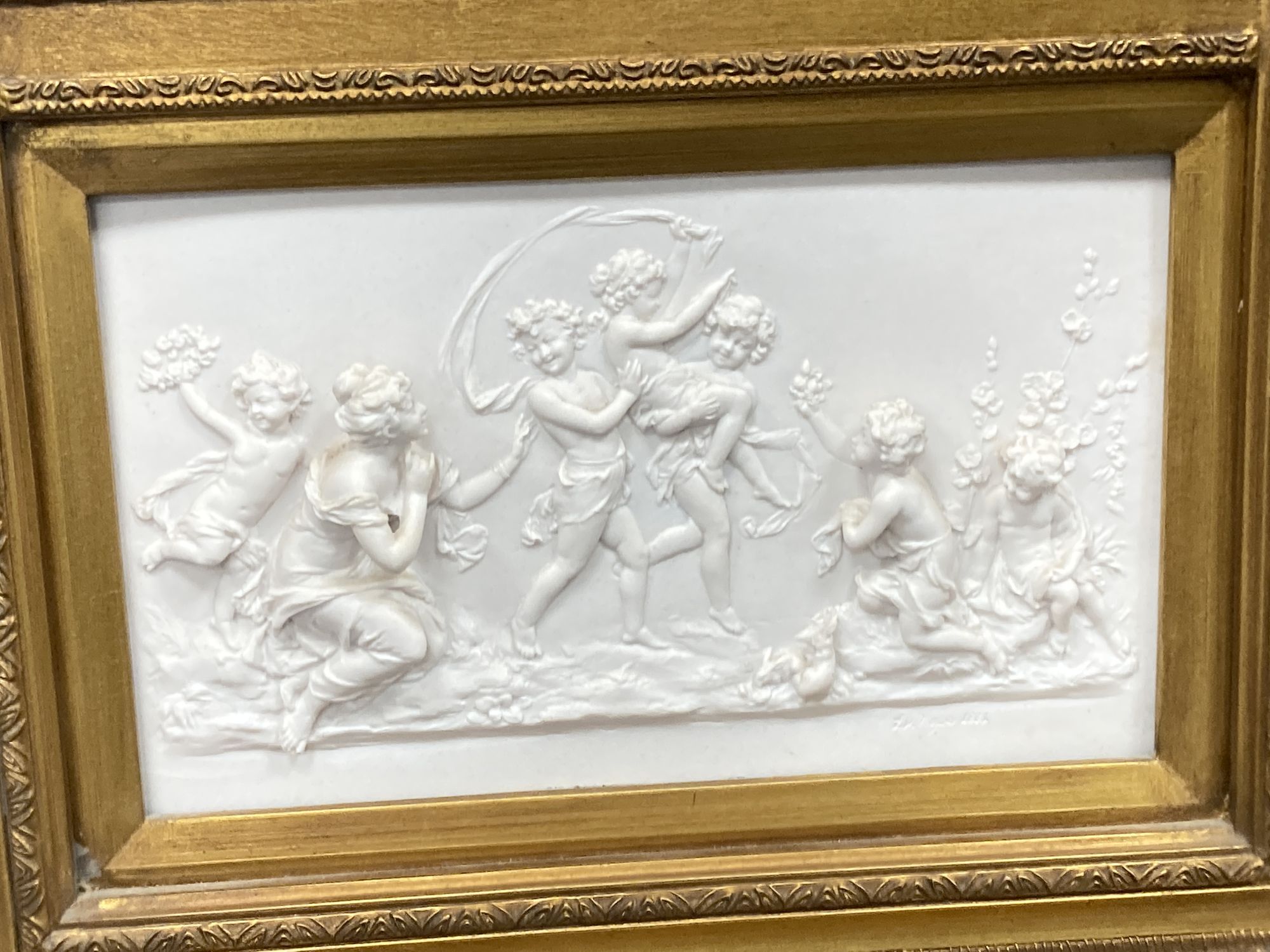 A gilt framed mirror, the base inset with a composition relief depicting putti at play, width 56cm, height 105cm